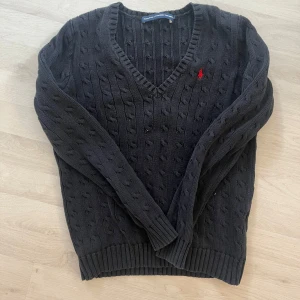 Svart stickad tröja från Ralph Lauren - Säljer en stilren svart stickad tröja från Ralph Lauren med v-ringning och det klassiska röda logotypbroderiet på bröstet. Perfekt för kyligare dagar och ger en tidlös look. Tröjan har långa ärmar och ribbade kanter.
