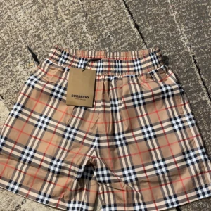 Rutig shorts från Burberry - Snygga rutiga shorts från Burberry i klassiskt beige, svart och rött mönster. Perfekta för sommardagar med sin lätta och bekväma passform. Elastisk midja för extra komfort.