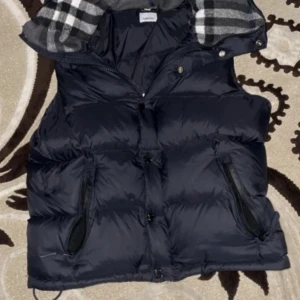 Svart burbbery väst - Snygg svart väst med dragkedja och knappar. Den har ett stilrent rutigt foder i grått och svart. 