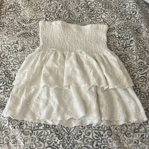 Vit kjol - Söt vit kjol med volanger och broderade detaljer. Perfekt för sommarens varma dagar. Den har en smockad överdel som ger en bekväm passform.