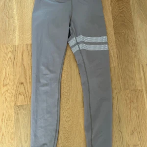 Beiga träningsbyxor från Stronger - Snygga beiga träningsbyxor från Stronger med vita randiga detaljer runt låret. Tillverkade i återvunnen polyester och elastan för en bekväm och stretchig passform. Perfekta för träning eller en aktiv vardag.