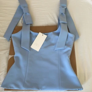 Zara top med rosetter - Jättesöta trendiga Zara toppen med breda axelband som knyts i rosetter och har en figurnära passform. Toppen är helt slutsåld på hemsidan. Helt ny med prislapp på, endast testad. Helt perfekt nu inför påsk och våren🐣Pris kan diskuteras💕