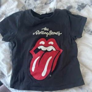 Svart Rolling Stones t-shirt från H&M - Säljer en cool svart t-shirt från H&M med det ikoniska Rolling Stones-loggan i rött och vitt på framsidan. Perfekt för små rockfans! 👶🎸