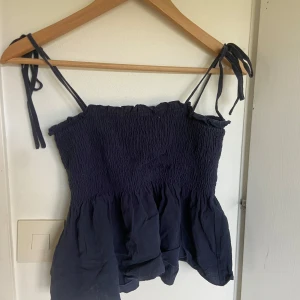 Mörkblå smockad linnetopp från SHEIN - Säljer en mörkblå smockad linnetopp från SHEIN med tunna axelband som knyts. Toppen är ärmlös och har en volangig nederdel. Perfekt för varma dagar och enkel att matcha med jeans eller kjol.