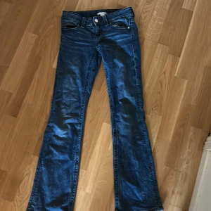 Blå bootcut Low waist  jeans från Gina Tricot - Snygga blå jeans från Gina Tricot i bootcut-modell. Klassisk femficksdesign med knäppning och dragkedja framtill samt dekorativa fickor bak. Perfekta för dig som gillar en tidlös jeansstil.