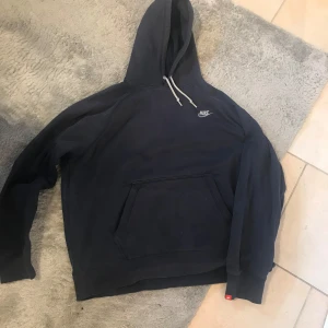 Mörkblå hoodie från Nike - Säljer en mörkblå hoodie från Nike i storlek XL. Tröjan har en klassisk huva med dragsko, magficka och Nike-logga på bröstet. Perfekt för en avslappnad stil och enkel att matcha med det mesta.