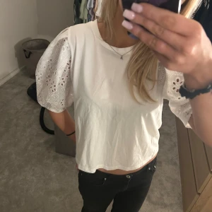 Vit topp med broderade puffärmar från Zara - Säljer en söt vit topp från Zara med korta puffärmar i broderad spets. Toppen har rund halsringning och är croppad i modellen. Perfekt för sommaren! Är i storlek M men passar andra som har XS/S🩷