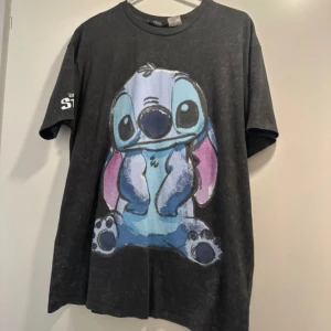 Svart Disney Stitch t-shirt från X-Side - Svart t-shirt med stort tryck av Stitch från Disney på framsidan. T-shirten har korta ärmar och rund halsringning. Materialet är mjuk bomull och tyget har en tvättad look. Disney Stitch-logga på ena ärmen.