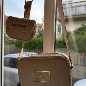 Beige axelväska från Valentino med quiltad design - Säljer en snygg beige axelväska från Valentino med quiltad struktur och guldfärgade detaljer. Väskan har två fack, ett större och ett mindre sidofack, justerbar axelrem. Perfekt för att bära det viktigaste med stil. Skriv för fler bilder eller diskutera pris