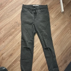 Svarta skinny jeans från Zara - Säljer ett par svarta skinny jeans från Zara med hög midja och slitningar vid knäna. Jeansen har klassisk femficksdesign, dragkedja och knapp framtill. Perfekta för en trendig och avslappnad look.
