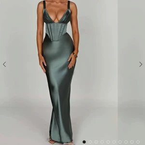 Mörkgrön långklänning med korsettliv - Säljer en elegant mörkgrön långklänning med smala axelband och djup v-ringning. Klänningen har ett figurnära korsettliv med snörning i ryggen och är tillverkad i ett glansigt satinliknande material. Perfekt för fest eller bal! Klänningen är helt oanvänd då den inte har passat mig! 