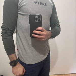 Grå och grön långärmad tröja från Levi's - Säljer en stilren långärmad tröja från Levi's med grå front och gröna ärmar. Tröjan har rund halsringning och klassisk passform. Perfekt för en avslappnad look.