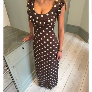 Brun långklänning med vita prickar och volang - Säljer en brun långklänning med vita prickar och volangdetaljer vid urringningen. Klänningen har ärmlös design, markerad midja med knytband bak. Heeelt otrolig till sommaren. Lappen finns kvar och är enbart testad. Säljer pga för liten. Storleken är XS/S