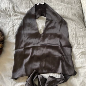 Svart halterneck topp med knyt från NA-KD - Säljer en svart halterneck topp från NA-KD i glansigt satinliknande material. Toppen har djup v-ringning och knytning i ryggen för en snygg passform. Perfekt för att lyfta vilken outfit som helst! Den är i storlek 34 men sitter som en 36. Köpte den för 300kr och den är endast använd ett fåtal gånger.😊