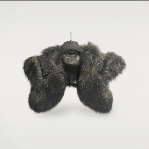 Svart pälsväst med nitar från Rock'n Blue - Säljer en svart pälsväst från Rock'n Blue med coola nitar på axelpartiet. Västen har en lyxig känsla med fuskpäls och detaljer i svart läderimitation. Perfekt för dig som vill sticka ut med en edgy stil.