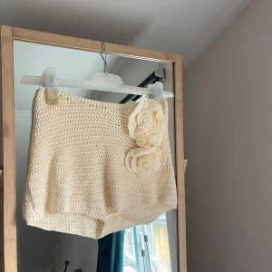 Stickade cremevita shorts med virkade blommor -  cremevita stickade shorts med två stora virkade blommor framtill.  Aldrig använda prislappen är kvar. Storlek S-M