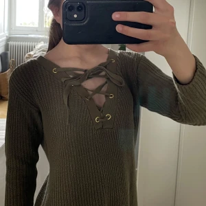 Olivgrön stickad tröja med snörning från Guess - Säljer denna jättefina olivgröna stickade tröjan från Guess med snygg snörning och guldfärgade öljetter. Den är I storlek XS & har inga som helst tecken på användning💗 Perfekt att ha över en bikini eller med ett par shorts nu till sommaren!!