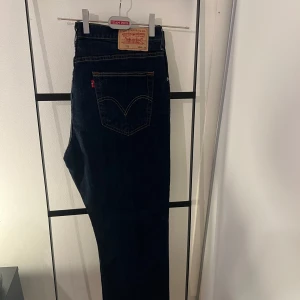 Levi's mörkblå jeansbyxor W38 L30 - Mörkblå jeansbyxor från Levi's med klassiska fem fickor och kontrastsömmar. Modellen har rakt snitt och läderpatch bak i midjan. Passar dig som gillar tidlös denimstil.