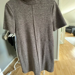 Grå/beige stickad klänning från Zara - Mysig grå stickad klänning från Zara med korta ärmar och hög hals. Klänningen har en rak passform. Enkel design utan synliga detaljer eller mönster.