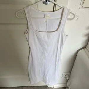 Vit ribbad klänning från H&M - Säljer en klassisk vit ribbad klänning från H&M i storlek XS. Toppen har breda axelband och rundad halsringning, perfekt att styla till olika outfits. Enkel och stilren design som passar året runt.