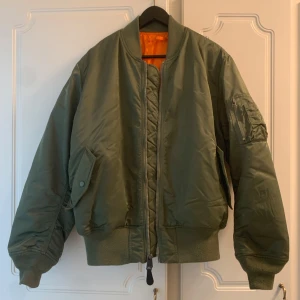 Alpha Industries, strl large - En klassisk MA-1 Heritage bomberjacka från Alpha Industries i färgen olivgrön, storlek large. Jackan har en orangefärgad insida. Nypris ca 2200kr. Fint skick förutom ett mindre brännmärke på vänster mudd, (VG se sista bild).  Du får den såklart nytvättad.   Postar samma dag som betalning gjorts! Har du frågor får du gärna höra av dig.  Mvh