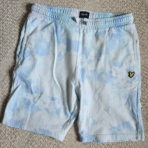 Ljusblå batikmönstrade shorts från Lyle & Scott - Säljer ett par ljusblå och vita shorts från Lyle & Scott med batikmönster och broderad logga framtill. Shortsen har resår i midjan och sidofickor samt en bakficka. Perfekta för sommardagar!