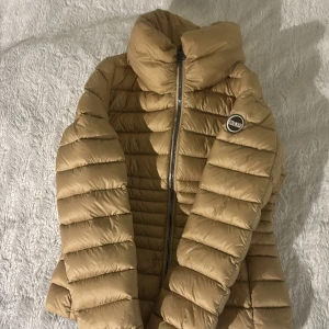 Beige pufferjacka från Colmar - Säljer en snygg beige pufferjacka från Colmar med hög krage och dragkedja framtill. Jackan har ett quiltat mönster och en rund Colmar-logga på bröstet. Perfekt för kyligare dagar och riktigt skön att bära. Nypris 3800kr