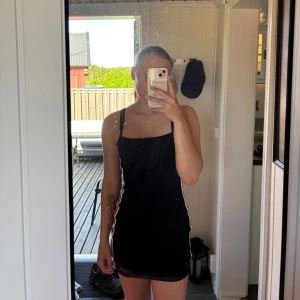 Svart tight kortklänning med ränder - Svart tight kortklänning med smala axelband och sportiga ränder i vitt och orange längs sidorna. Enkel och stilren design som passar perfekt för sommaren.