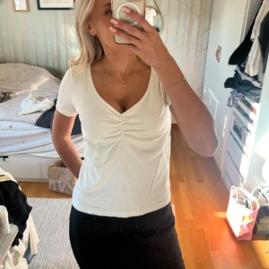 Vit v-ringad topp med rynk framtill - Säljer en vit (benvit) topp med korta ärmar och v-ringning. Toppen har en snygg rynkdetalj framtill vid bysten och är i ett mjukt bomullsmaterial. Perfekt till jeans eller kjol för en enkel och stilren look. 