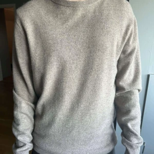 Beige stickad tröja i kashmir från John Henric - Säljer en stilren beige stickad tröja i mjuk kashmir. Tröjan har rund halsringning och långa ärmar med ribbade muddar. Perfekt för lager-på-lager och passar till många olika outfits. Mycket bra sick, använd ett fåtal gånger. Nypris 2200kr