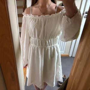 Vit offshoulder klänning från H&M Divided - Säljer en söt vit offshoulder klänning från H&M Divided med långa ärmar och resår i midjan. Klänningen har volangdetalj upptill och är tillverkad i ett lätt, strukturerat tyg. Perfekt för varma dagar eller speciella tillfällen! Läs gärna bio!💘