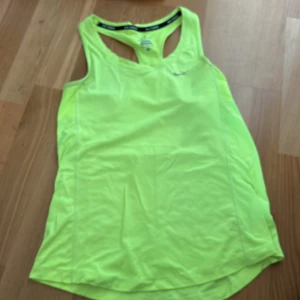 Neongul träningstopp från Nike - Säljer en neongul ärmlös träningstopp från Nike med Dri-FIT-material. Perfekt för intensiva träningspass, med brottarrygg och diskret Nike-logga på bröstet. Lätt och snabbtorkande material.