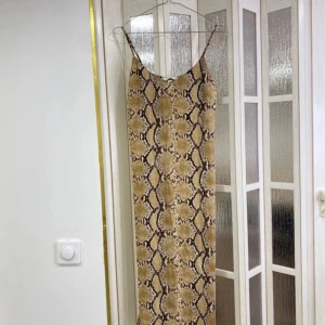 Beige långklänning med ormmönster från H&M - Säljer en beige långklänning med smala axelband och trendigt ormmönster från H&M. Klänningen har en rak passform och är perfekt för dig som gillar djurmönstrat och vill sticka ut.