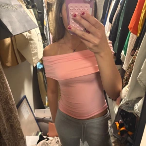 Ljusrosa offshoulder topp - Säljer en ljusrosa offshoulder topp i stretchigt material. Toppen har en tight passform och är axelbandslös med bred volangkant upptill. Perfekt för dig som vill ha en enkel men snygg topp till sommaren! Helt ny, köpte men använde aldrig. Skriv för fler bilder elle info🥰