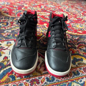  New Balance sneakers - Säljer ett par höga New Balance sneakers i svart och rött med svart sula. Skorna har snörning, tydlig New Balance-logga på sidan och baksidan. Perfekta för dig som gillar sportig stil. Passar både man/kvinna. Knappt använt som nya. 