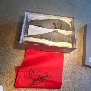 Beiga sneakers från Christian Louboutin - Säljer ett par beige sneakers från Christian Louboutin med klassisk röd sula. Skorna har snörning, rund tå och är tillverkade i mocka. Kommer med originalkartong och röd dustbag. Storlek 45 och sick 8-10