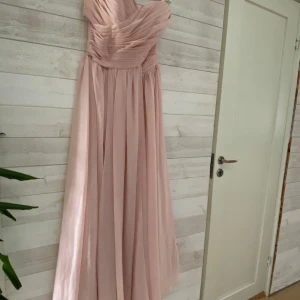Ljusrosa långklänning med draperad överdel - Säljer en  ljusrosa långklänning med draperad, axelbandslös överdel och markerad midja. Kjolen är mjukt fallande och klänningen passar perfekt till bal eller fest. Klänningen är stl M men upplevs som en s när vi provar den så liten i stl. 