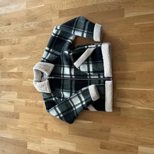 Rutig teddyjacka från Vaillent - Säljer en svart och vit rutig teddyjacka från Vaillent i storlek S. Jackan har dragkedja, mjukt teddyfoder och detaljer i beige. Perfekt för kyliga dagar och har en klassisk krage samt långa ärmar. Väldigt stilig priset är inte hugget u sten 