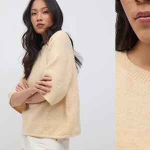 Beige stickad tröja från Gina  - Mysig beige stickad tröja från COS med rund halsringning och korta, vida ärmar. Tröjan har en avslappnad passform och är tillverkad i ett mjukt material som passar perfekt för lager-på-lager-stil.