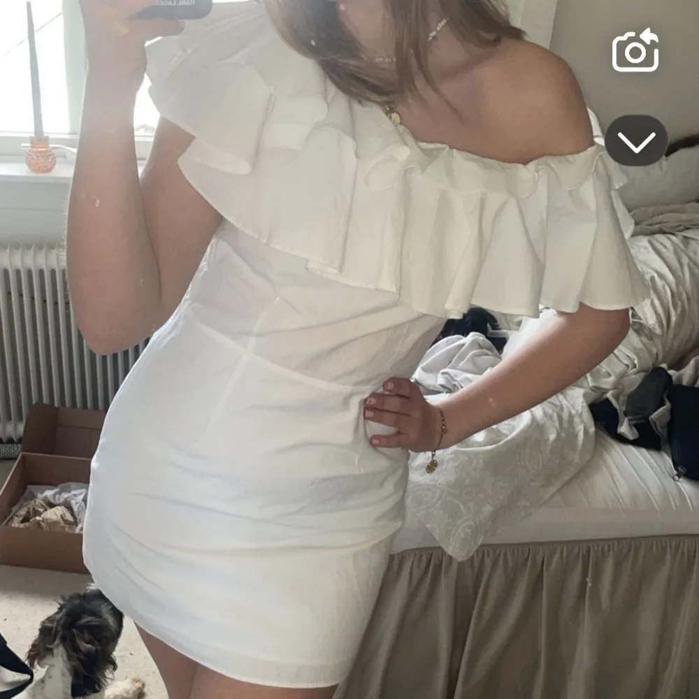 Säljer en vit kortklänning med offshoulder och stor volangdetalj över axlarna. Klänningen har en figurnära passform och dragkedja i sidan som har gått sönder i sömmarna, men väldigt lätt att sy. Perfekt för studenten eller sommarens tillfällen när du vill sticka ut lite extra.. Mekot.