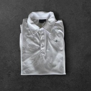Vit golf pikétröja från Cross Sportswear - Säljer en klassisk vit pikétröja från Cross Sportswear i storlek M. Tröjan har korta ärmar, krage och knappar framtill. Perfekt för en sportig och stilren look. Materialet är lätt och andas bra.