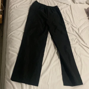 Svarta vida byxor med resår i midjan - Säljer ett par svarta byxor med breda ben och resår i midjan. Perfekta för en avslappnad stil och enkla att matcha med olika toppar. Materialet känns mjukt och bekvämt.