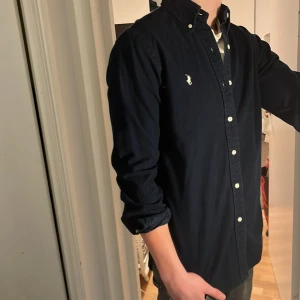 Ralph Lauren Skjorta - Tja säljer en Ralph lauren skjorta i färgen mörkblå och i storlek S passar 170-180 cm ungefär. Nypris 1595 KR mitt pris 299 KR. Inga defekter som hål eller fläckar. Skriv vid frågor eller funderingar.
