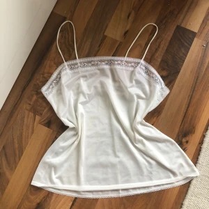 Vit linnetopp med spets🌸 - Säljer en söt vit linnetopp med tunna axelband och spetsdetalj längs överkanten. Toppen är lätt och luftig, perfekt för varma dagar eller som lager under andra plagg. Mjukt material och förmodligen vintage❣️