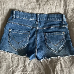 Lågmidjade jeans shorts - Säljer ett par klassiska blå jeansshorts från Pull&Bear med rå, fransig kant och femficksmodell. Shortsen har normal passform, låg midja och snygga slitningar framtill. Perfekta för varma dagar! De är i nyskick och endast använda fåtal gånger. Midjemått rakt över: 34, men stretchiga! Kontakta gärna vid frågor eller funderingar❤️Shprtsen är i storlek 146 men sitter som xxs/xs