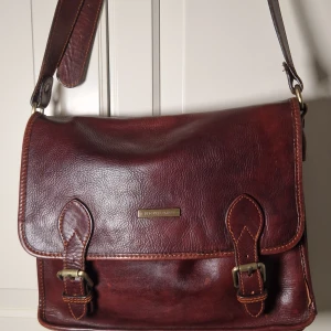 Brun axelväska i skinn  - Hej!  Säljer här en stilren kuvertväska som passar lika bra på jobbet som vid festligheter.  Mycket bra kvalitet och lädret är 28 mars smörjt och impregnerat.   Inne i väskan finns små fläckar från en grön bläckpenna men det syns endast om man anstränger sig och har bra ljus.  Bilder kan skickas på detta.