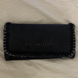 Svart plånbok från Stella McCartney - Säljer min älskade Stella McCartney plånbok då den inte kommer till användning längre. Plånboken har flera kortfack, myntfack med dragkedja och ett fönsterfack. Perfekt för att hålla ordning på kort och kontanter.