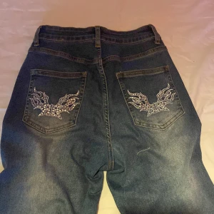 Blå jeans med broderade fickor - Säljer ett par blå jeans med snygga broderade detaljer på bakfickorna. Klassisk femficksmodell med normal passform och bootcut. Perfekta för dig som vill ha något unikt i garderoben!
