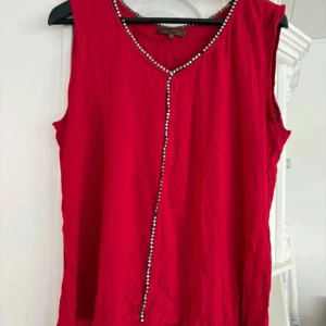 Röd ärmlös topp med pärldetaljer från Honey - Säljer en röd ärmlös topp från Honey med dekorativa pärlor längs ringningen och framtill. Toppen har en lös passform och är perfekt för dig som vill ha något enkelt men ändå med en snygg detalj. Saknas några stenar på några ställen annars bra, storlek M