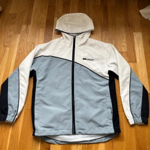 Ljusgrå vindjacka från Reebok - Snygg vindjacka från Reebok i ljusgrått och vitt med svarta detaljer.💗Det står att storleken är 12/40 men sitter som L. Jackan har sportig design, och perfekt för utomhusaktiviteter eller en street styled look! Inga defekter och i bra skick. Skriv om ni har frågor💗